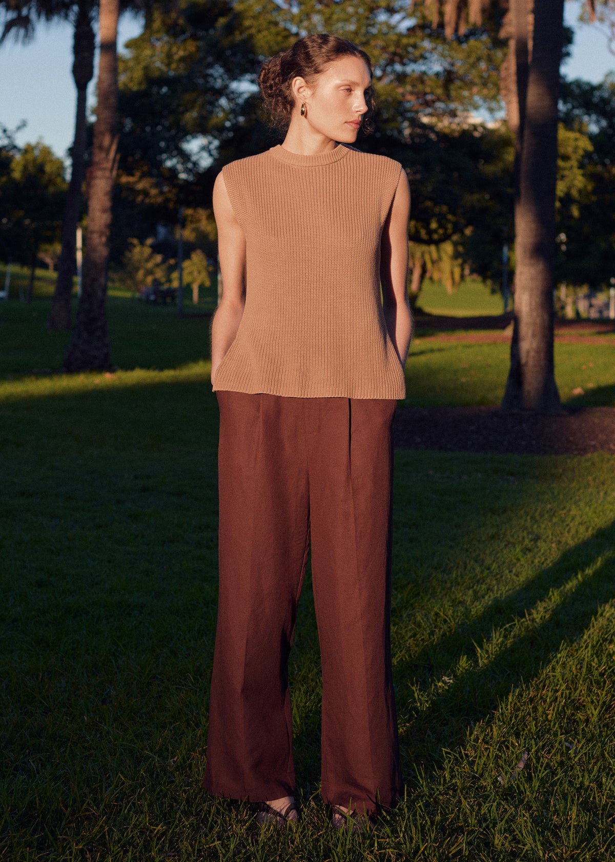Model wearing Taupe Cotton Blend Knit Tank Top with a relaxed fit and a crew neckline, photographed on grass and palm trees.