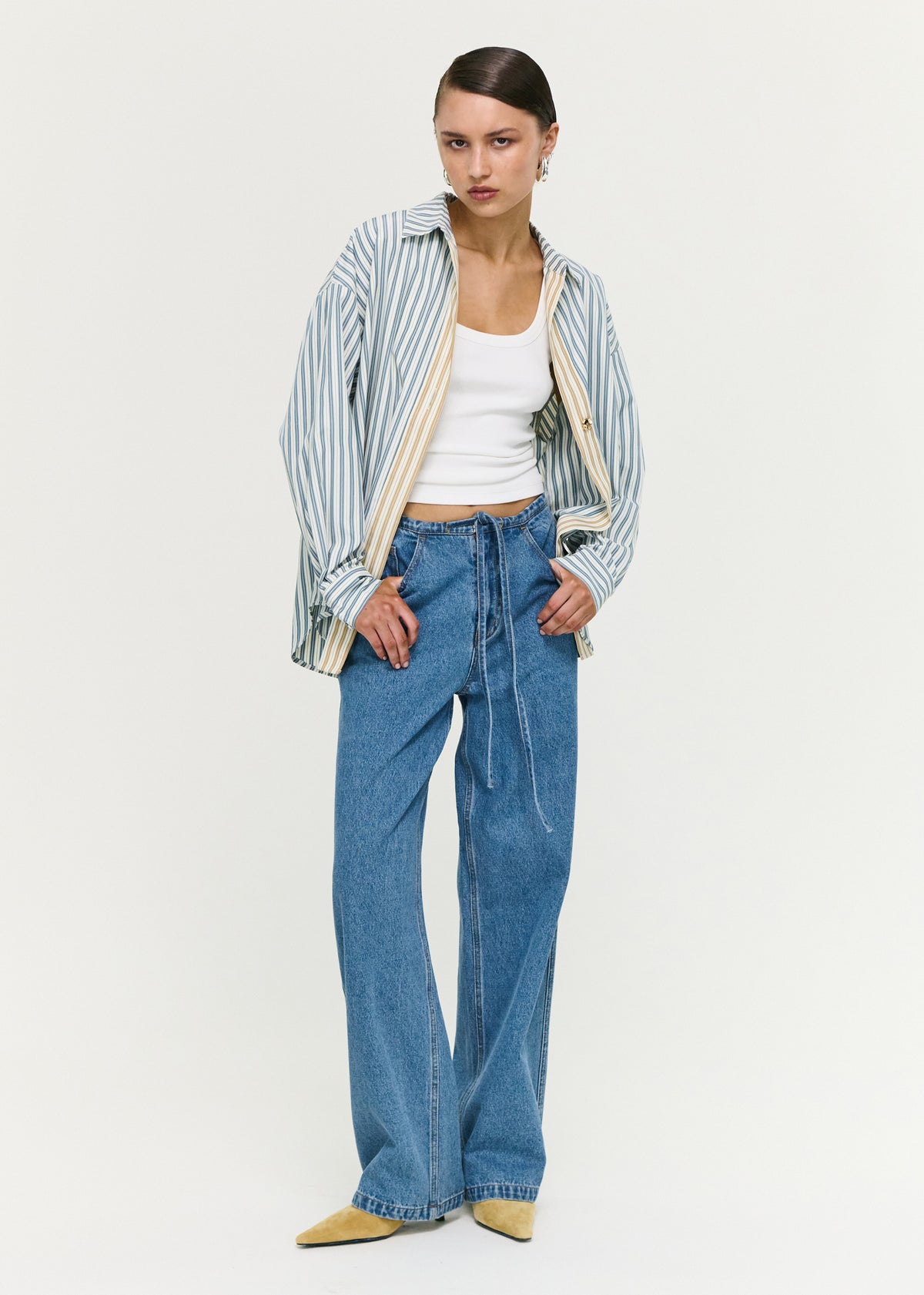 Model wearing Tie Waist Detail Mid Rise Jeans with a rigid denim fabrication and a mid-rise waist.