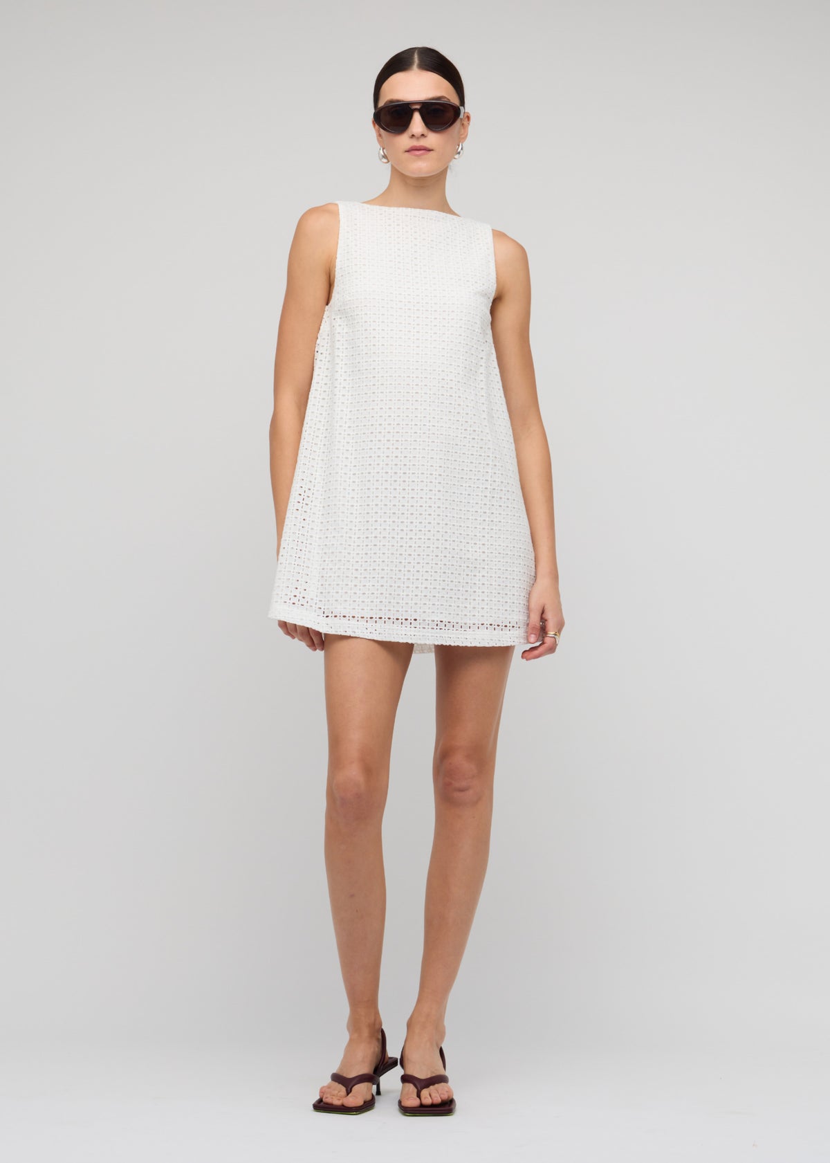 Model wearing White Broderie Mini Shift Dress, showing a mini shift silhouette and a high neckline with sleeveless cut.