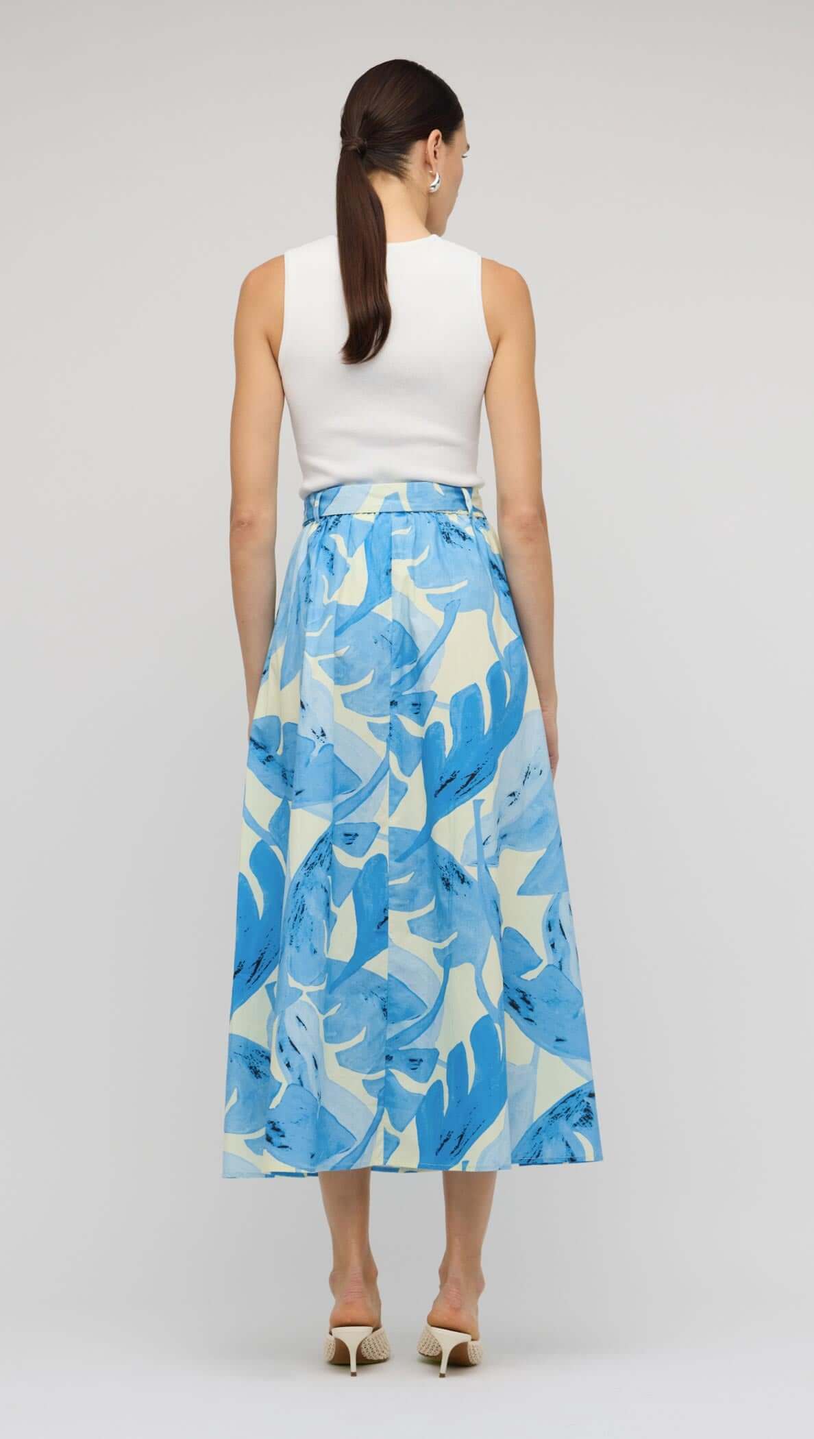 Back view of model wearing White Cut-Out Sleeveless Knit Top paired with a floral maxi skirt.