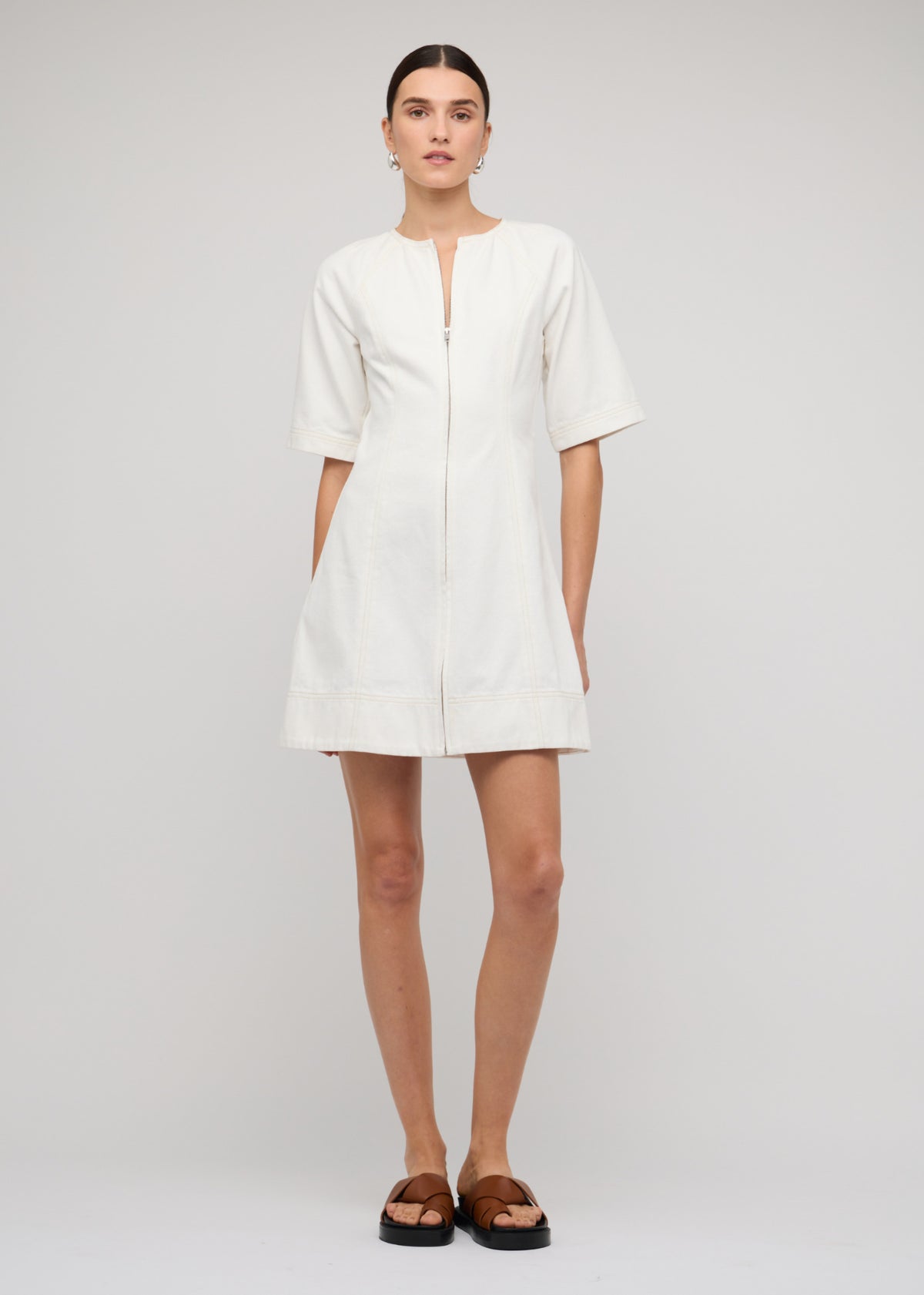 Model wearing White Denim Mini Dress With Front Zip with a white denim finish and short sleeves.