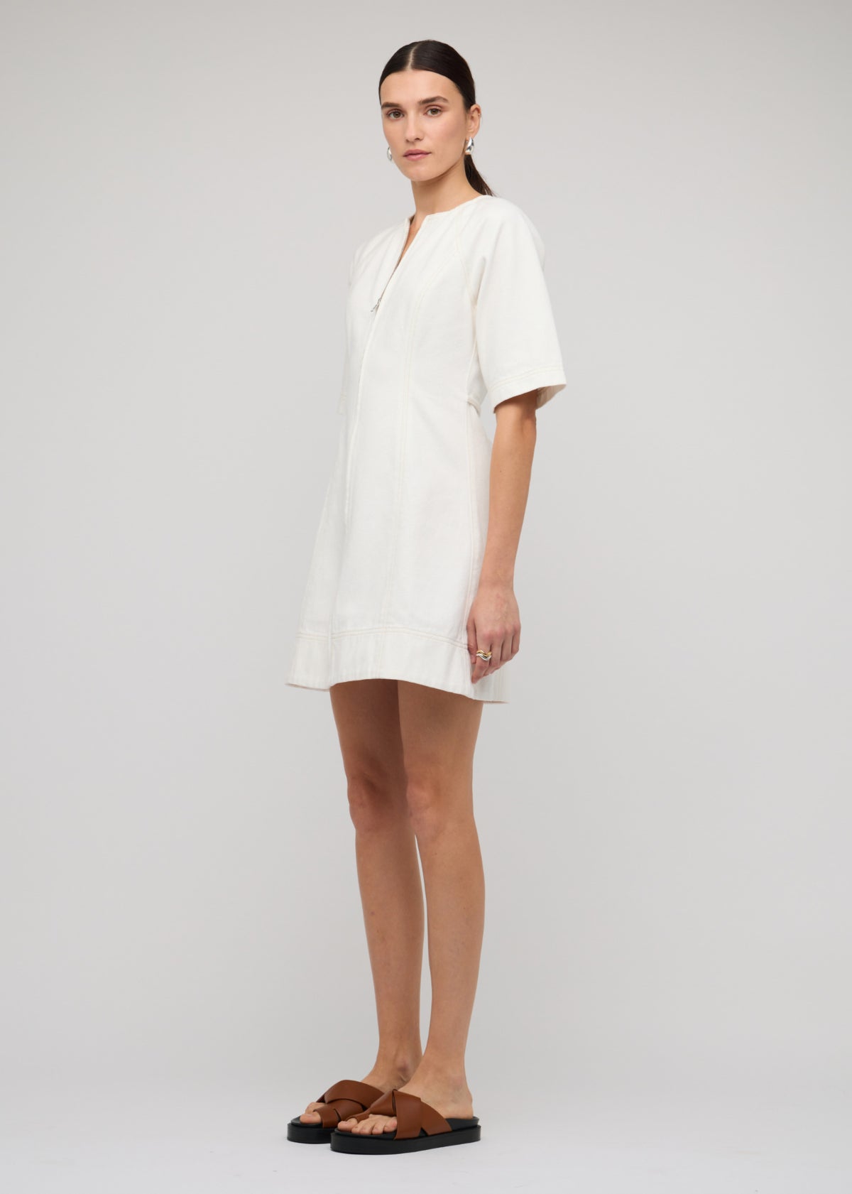 Side view of the White Denim Mini Dress With Front Zip, showing a mini length and a white denim finish.
