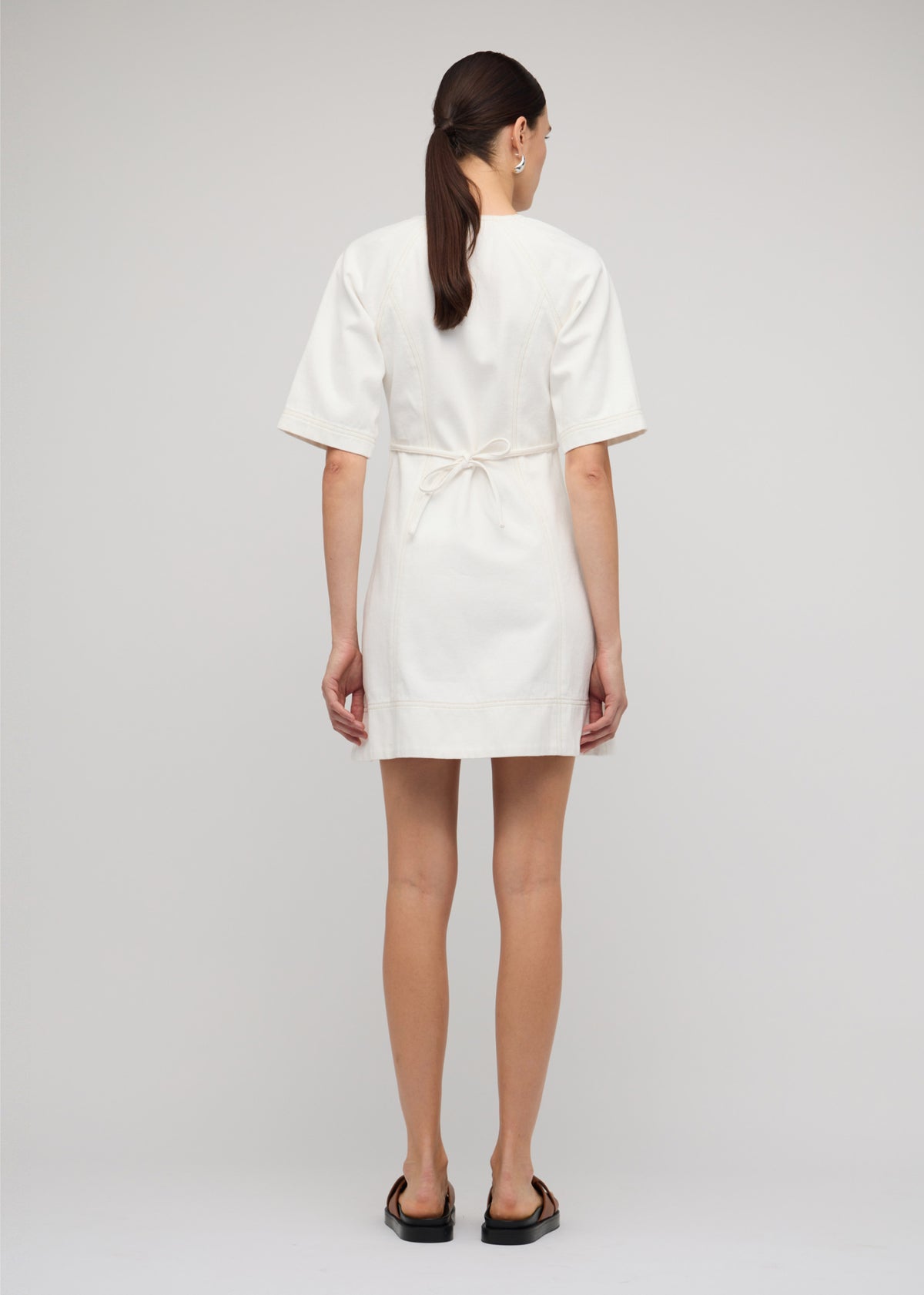 Back view of the White Denim Mini Dress With Front Zip with a centre-front exposed zip and a tie-back waist detail.