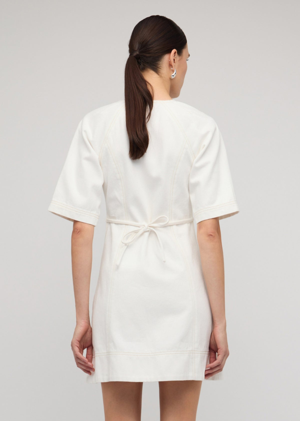 Back view of the White Denim Mini Dress With Front Zip, showing a centre-front exposed zip and a tie-back waist detail.