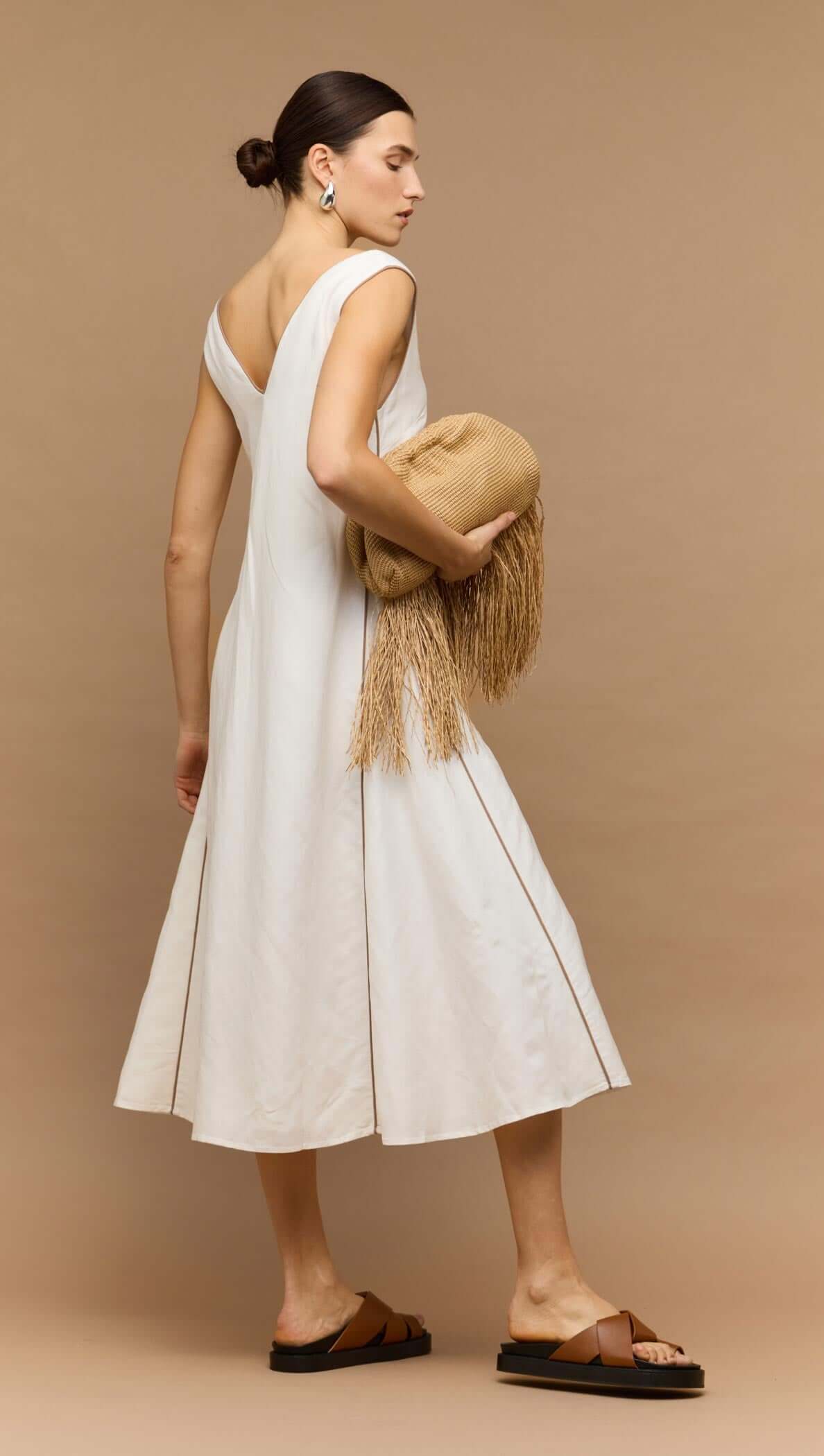 Model wearing a White Godet Linen Midi Dress, featuring a V-neckline and a softly flared skirt, paired with a stylish clutch.