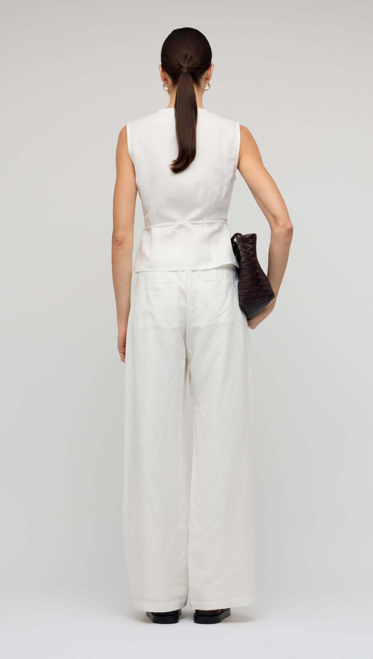 Back view of a model wearing the White Sleeveless Linen Wrap Top with wide-leg pants, showcasing a minimalist outfit.