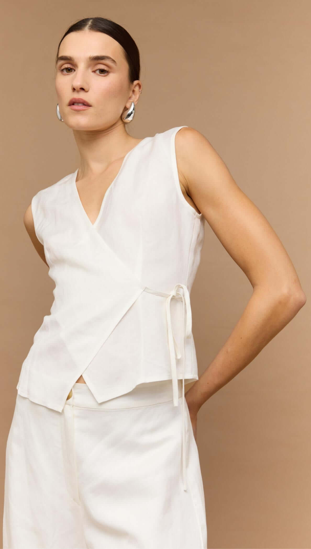 Woman wearing a White Sleeveless Linen Wrap Top with deep V-neckline and adjustable tie waist.