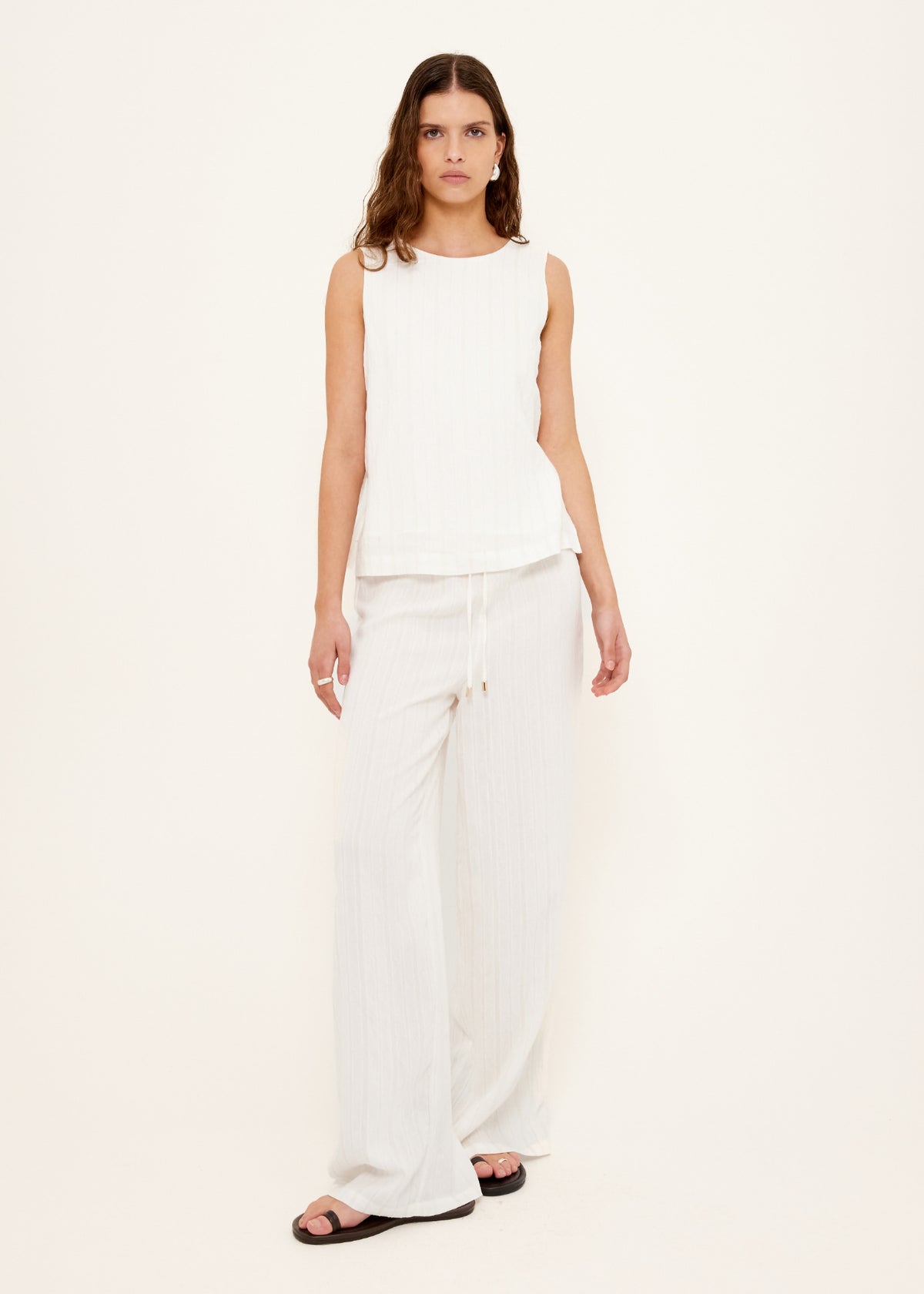 Model wearing White Tie-Side Top with a lightweight textured fabric and a sleeveless relaxed fit, turned to the side.