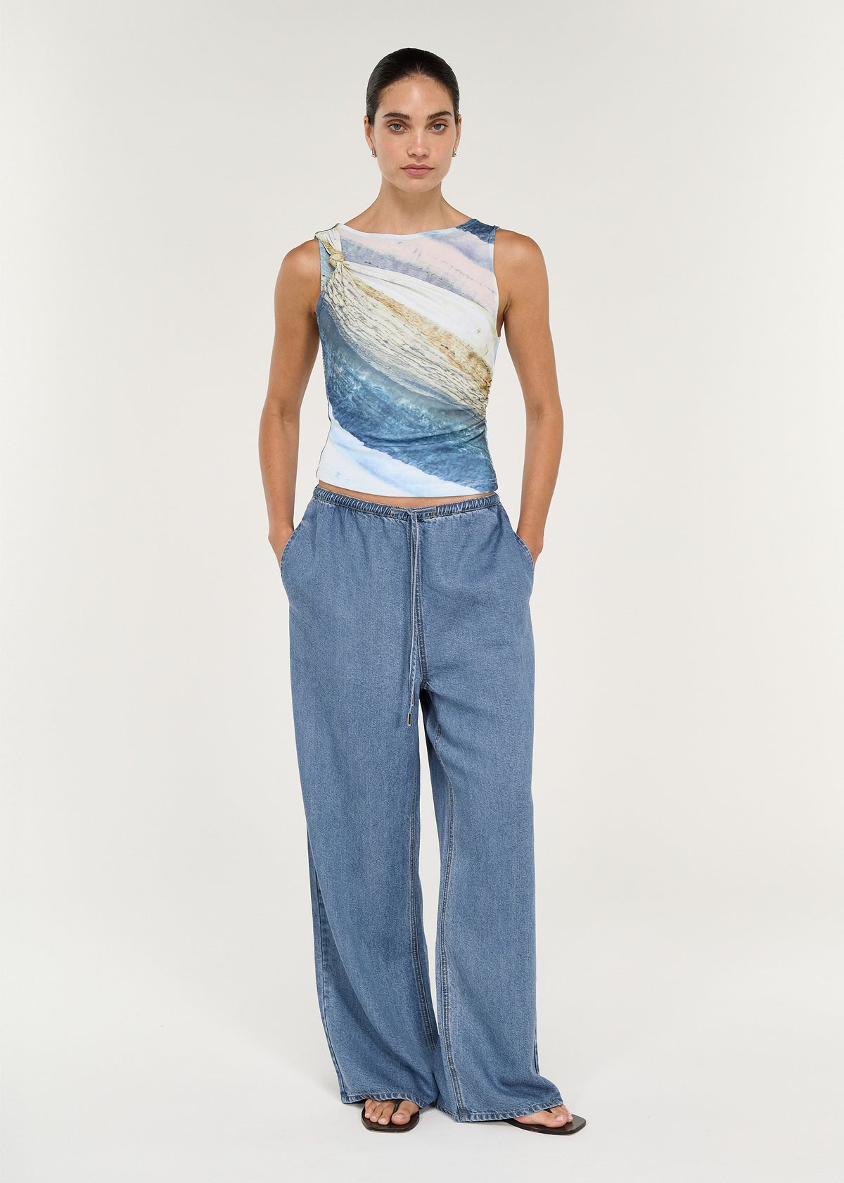 Model wearing the Sleeveless Mesh Twist Top in Ocean Tide, styled with relaxed denim pants.